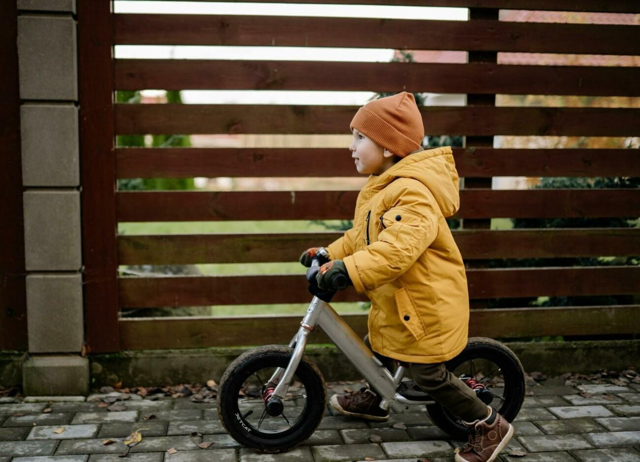 En liten pojke cyklar vid staket.