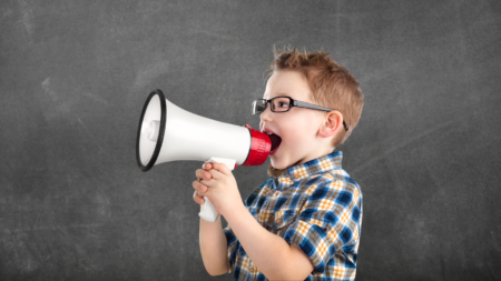 Nuori poika huutaa megafoniin liitutaulun edessä.
