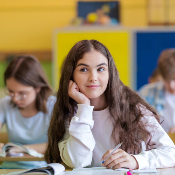 Tre ungdomar sitter i ett färgglatt klassrum, en eftertänksam flicka i förgrunden.