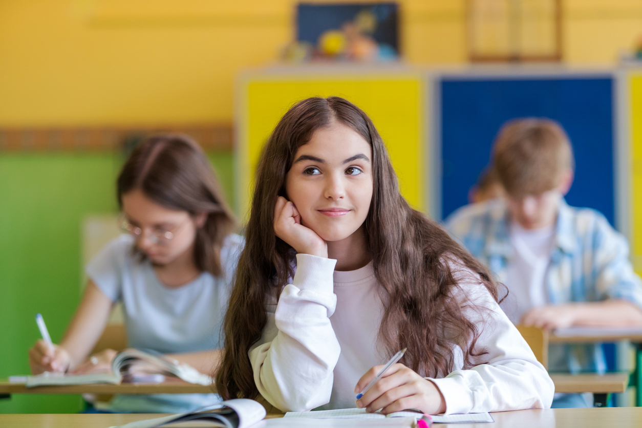 Tre ungdomar sitter i ett färgglatt klassrum, en eftertänksam flicka i förgrunden.