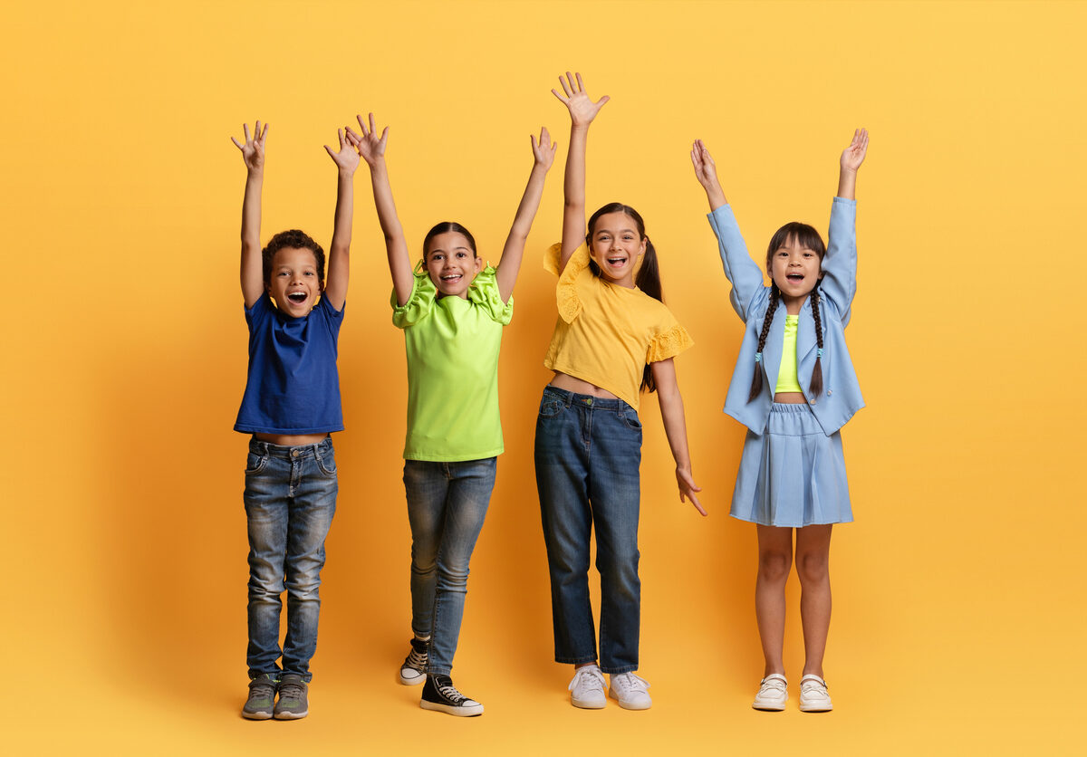 Neljä lasta kädet ilmassa keltaista taustaa vasten.