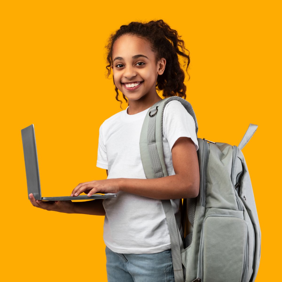 Tyttö hymyilee reppu selässä ja läppäri kädessä.