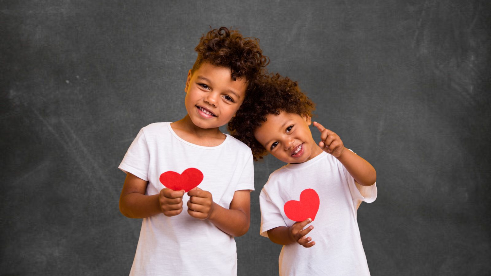 Två barn håller pappershjärtan i händerna och ler.
