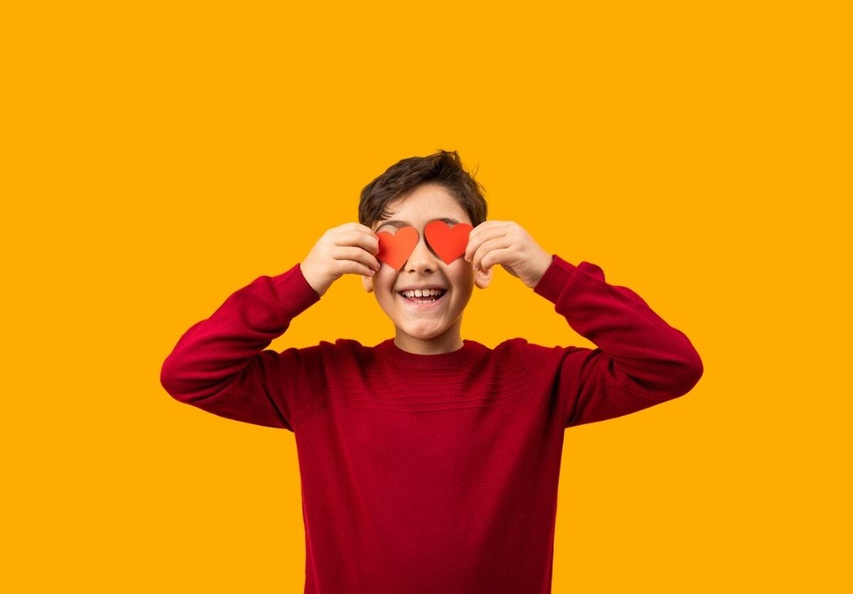 Pojken ler och håller pappershjärtan framför ögonen.